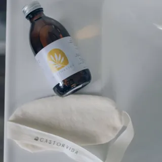 Brown bottle with Castorvida label next to a cream fabric pouch with Castorvida text.
