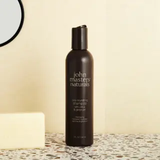 Brown bottle of John Masters Naturals shampoo with citrus and geranium, next to a soap bar.