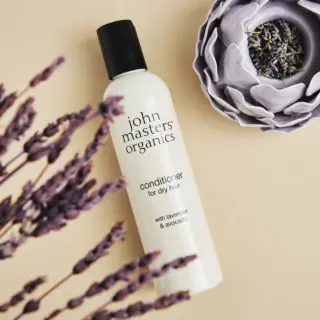 John Masters Organics conditioner for dry hair with lavender and avocado, next to lavender flowers.