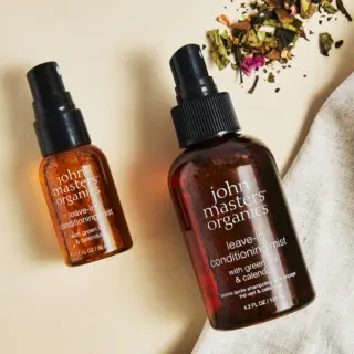 Two bottles of John Masters Organics leave-in conditioning mist on a beige surface.