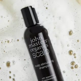Black bottle of John Masters Organics scalp shampoo on foamy surface.