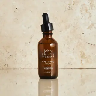 Brown bottle of John Masters Organics scalp purifying serum with dropper on stone background.
