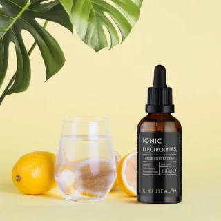 Brown bottle of ionic electrolytes, glass of water, lemons, and green leaves on yellow background.