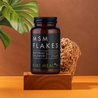 MSM Flakes jar, 200g, on wooden block with plant and stone background.