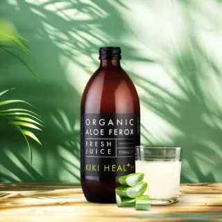 Brown bottle of organic aloe ferox juice, glass, and aloe slices on wooden surface.