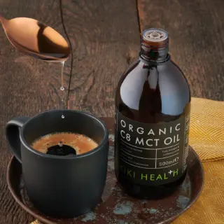 MCT oil bottle beside a mug of coffee on a wooden table.