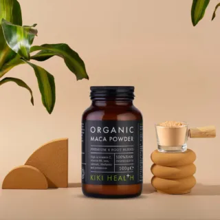 Organic Maca Powder jar, 100g, with a wooden scoop and green leaves in the background.