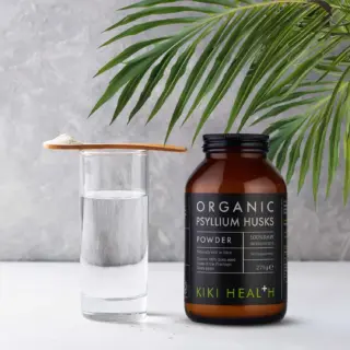 Kiki Health Organic Psyllium Husks jar beside a glass of water and wooden spoon with powder.