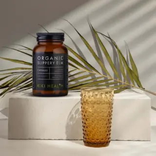 Organic Slippery Elm capsules bottle on stone block with amber glass and palm leaf.