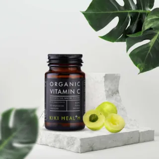 Kiki Health Organic Vitamin C bottle with sliced amla on marble surface, surrounded by green leaves.