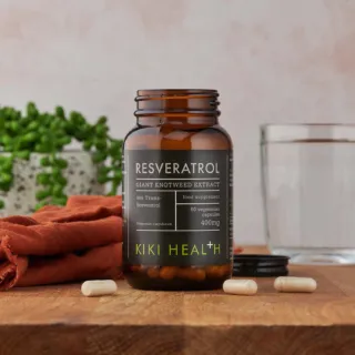 Kiki Health Resveratrol supplement bottle on wooden table with capsules and glass.