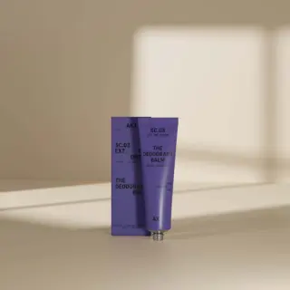 Purple deodorant balm tube and box with text, in soft light.