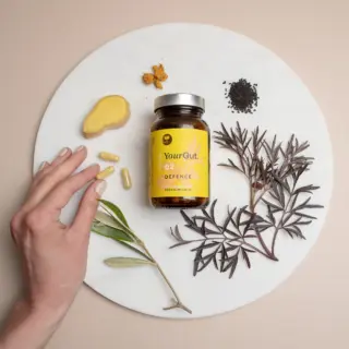 YourGut 02 Defence supplement bottle with herbs, ginger, and capsules on a round white surface.