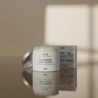 AKT foaming body scrub jar and box on reflective surface.
