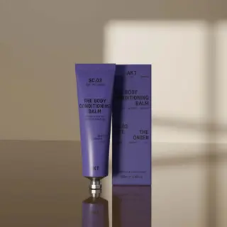 Purple tube and box of AKT SC.03 The Body Conditioning Balm on a reflective surface.
