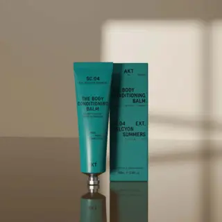 Green tube and box of AKT SC.04 Body Conditioning Balm on reflective surface.