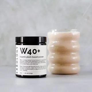 W40+ organic plant-based powder jar next to a wavy glass filled with a beige smoothie.