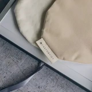 Beige and cream fabric bags with "CASTORVIDA" label in a box on a textured surface.