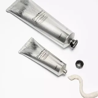 Two silver tubes of Olverum Body Polish on a white background, with cream and a black cap.