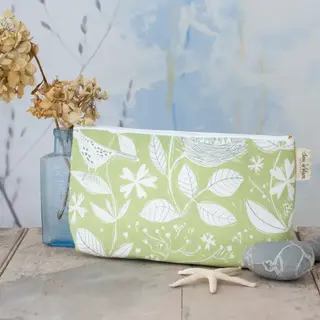 Green floral toiletry bag on wooden table with dried flowers and stones.