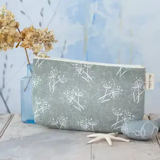 Green pouch with white floral pattern, beside dried flowers in a blue vase and grey stones.