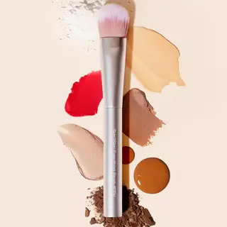 Makeup brush with various coloured powders and creams on a beige background.
