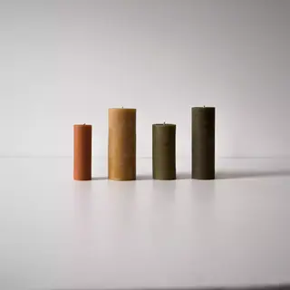 Four pillar candles in varying heights and earthy tones on a white surface.