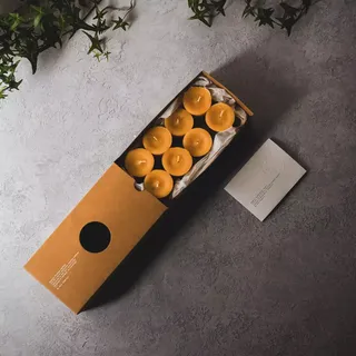 Box of eight yellow candles on grey surface with green ivy.