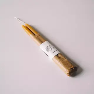 Two yellow candles wrapped in brown paper with a white label on a light surface.
