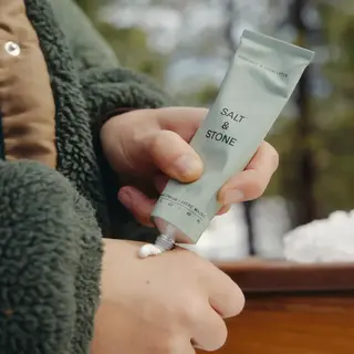 Person applying Salt & Stone hand cream outdoors.
