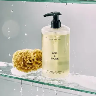 Salt & Stone body wash with sponge on wet glass shelf.