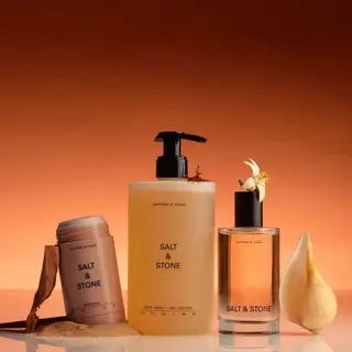 Salt & Stone skincare products on reflective surface, orange background.
