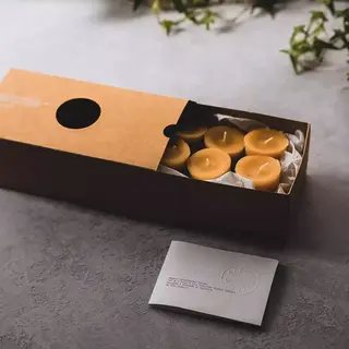 Brown box with six yellow candles, card with embossed text, and green ivy in the background.
