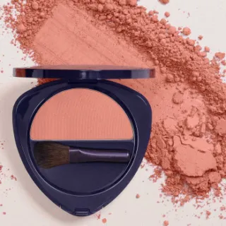 Open compact with peach blush and brush, surrounded by loose powder.