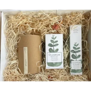 Gift box with Olverum bath oil, pillow mist, and a brown cylindrical package on straw.