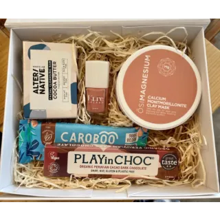 Gift box with clay mask, cleansing bar, nail polish, and vegan chocolate bars on straw filling.