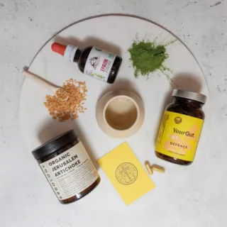 Supplements, flax seeds, green powder, and a small bowl on a round white surface.