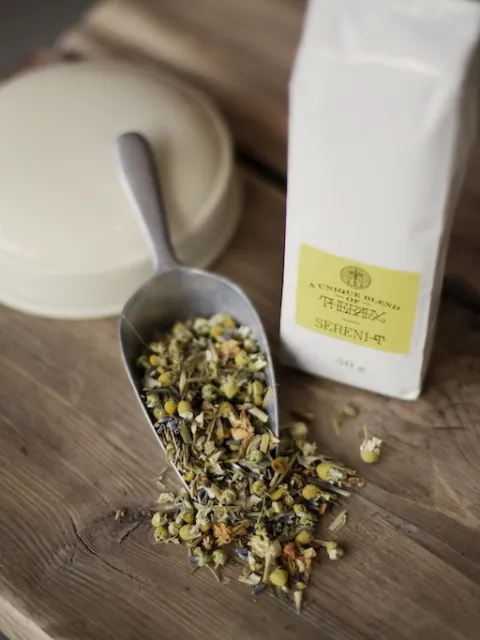 Herbal tea blend with scoop and white packet on wooden table.