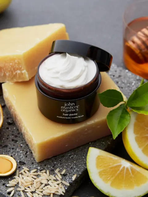 Hair paste jar on soap blocks with lemon, honey, oats, and leaves on a dark surface.