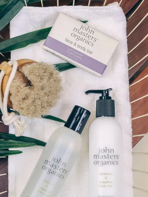 Skincare products and brush on a towel with green leaves.