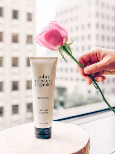 Tube of John Masters Organics hair milk with a pink rose held nearby.