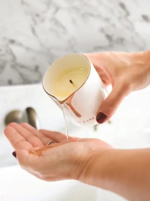 Hands pouring melted candle wax into palm over a marble sink.