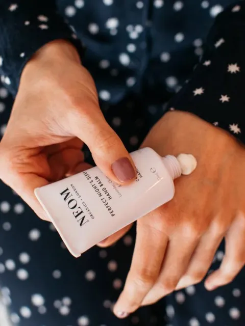 Hands applying NEOM hand balm in a star-patterned outfit.