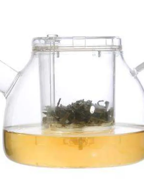 Clear glass teapot with infuser, containing green tea leaves and brewed tea.
