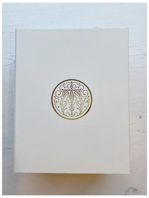 White box with ornate gold circular emblem on a light wooden surface.