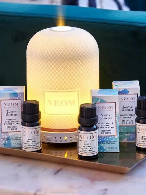 NEOM diffuser with essential oils on a tray, set against a green sofa.