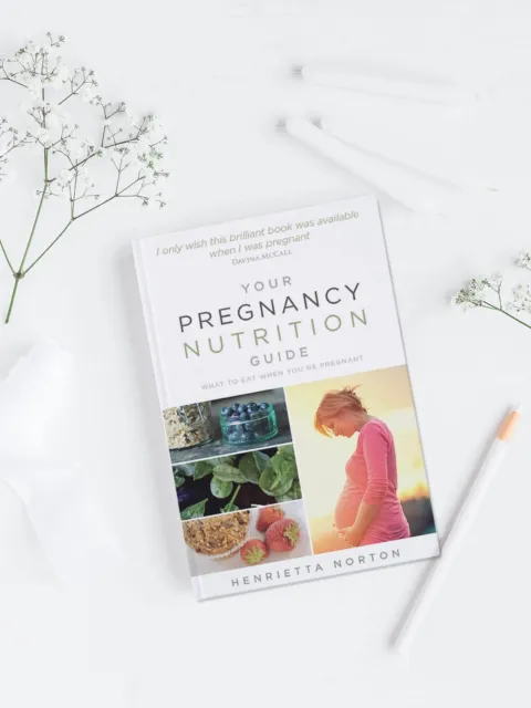 Pregnancy nutrition book on white surface with flowers and a pen.