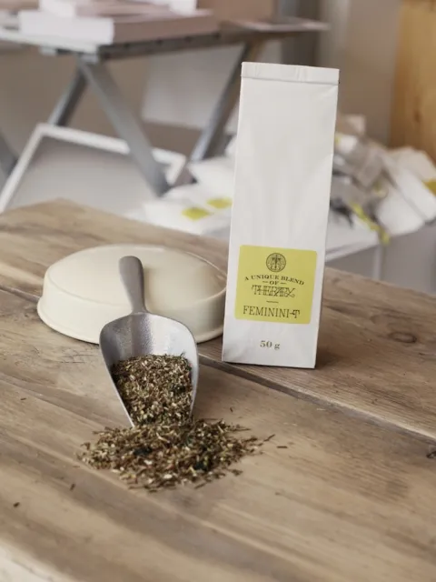 Herbal tea blend labelled "FEMININI-T" with a scoop on a wooden table.