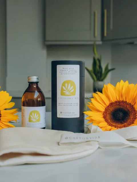 Castor oil bottle, cylindrical box, cloth, and two sunflowers on a kitchen counter.