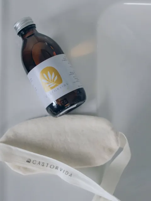Brown bottle with Castorvida label next to a cream fabric pouch with Castorvida text.